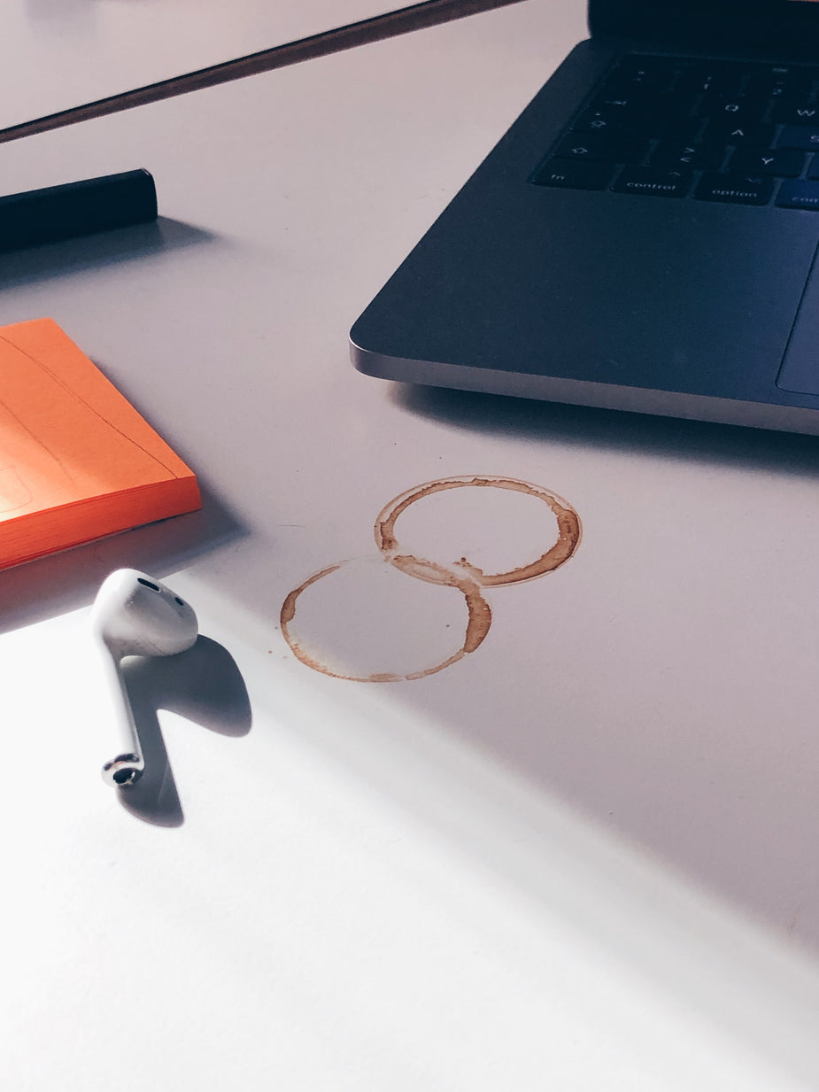 Auf dem Bild ist ein Schreibtisch zu sehen, auf dem ein Notebook steht und InEar-Kopfhörer liegen mit zwei runden Kaffeeflecken vom Tassenboden