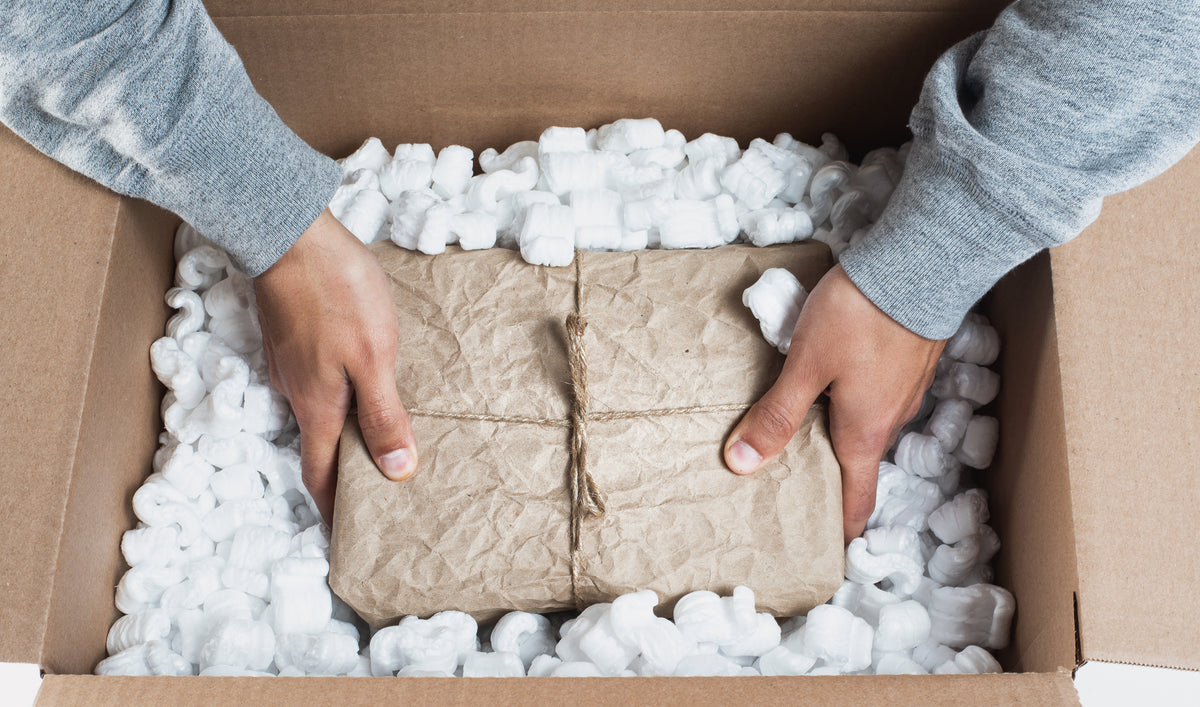 Zu sehen ist das Einpacken eines kleineren Päckchens in einen großen Karton zum Versenden